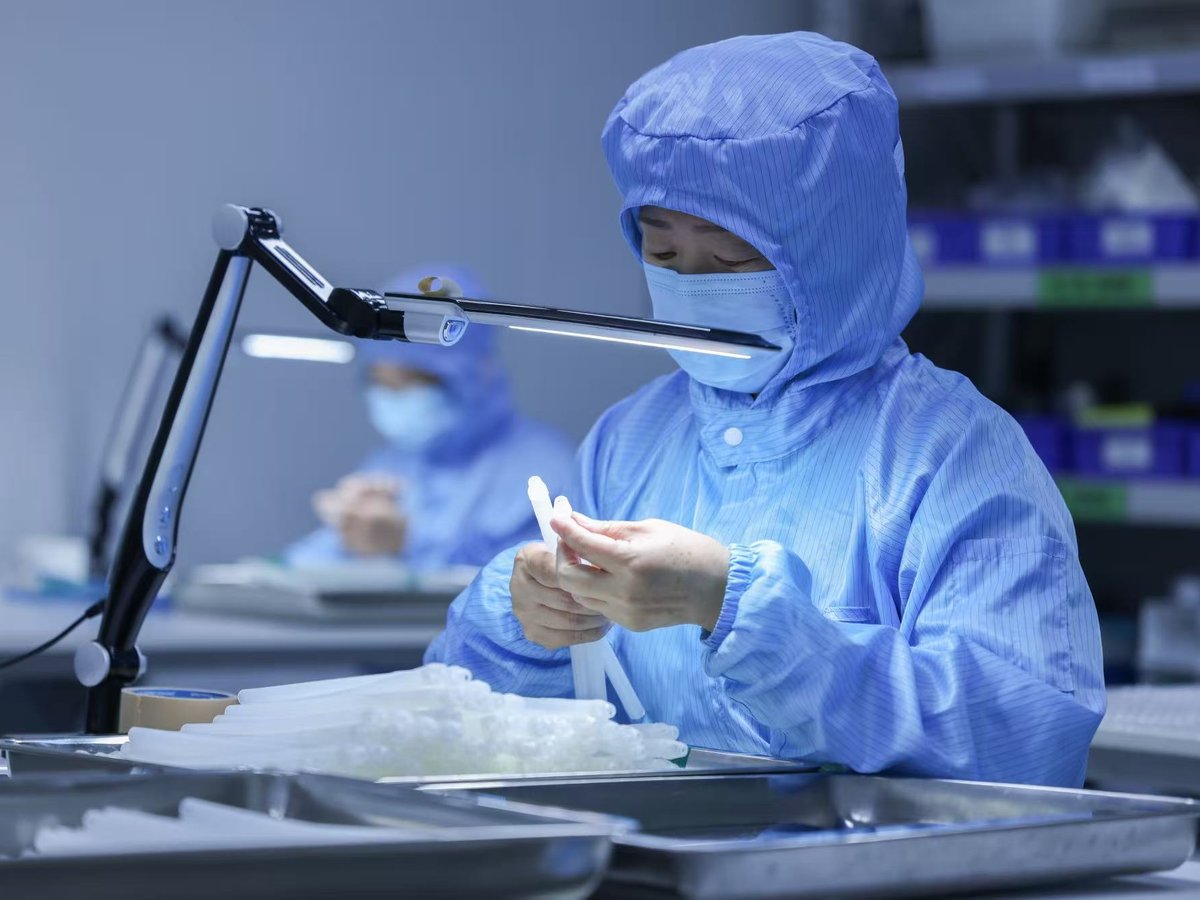 クリーンルームで防塵服を着た作業者が医療用チューブを検査している様子